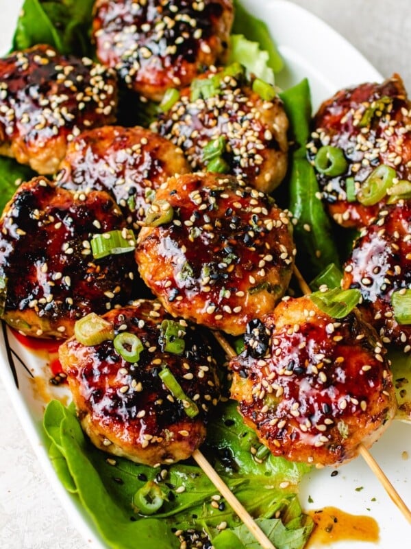 Feature image shows Japanese chicken meatballs (Tsukune) brushed with yakitori sauce and served on a white plate.