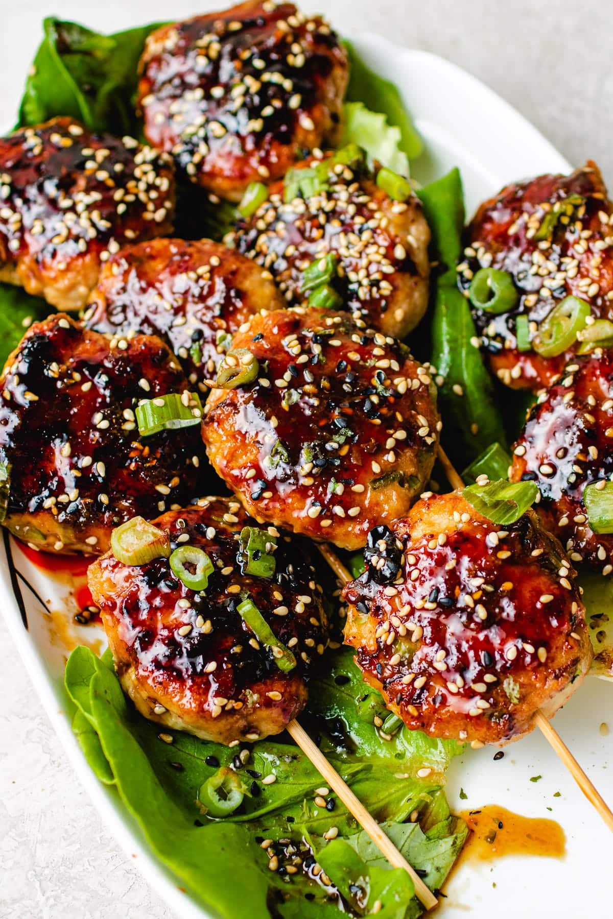 Feature image shows Japanese chicken meatballs (Tsukune) brushed with yakitori sauce and served on a white plate.