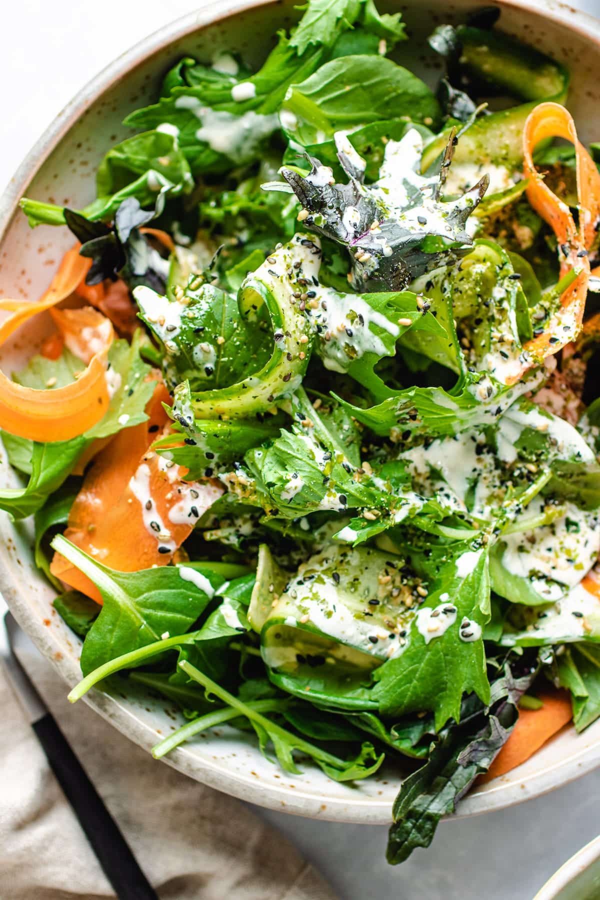 A close shot shows tatsoi greens with green, red, and purple leafy greens served in a white plate with dressing on top.