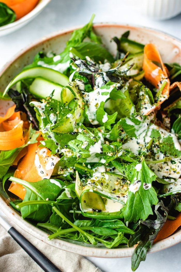 A side shot shows tatsoi mixed with Asian baby greens with shaved carrot and cucumber served in a big salad plate with dressing on top.