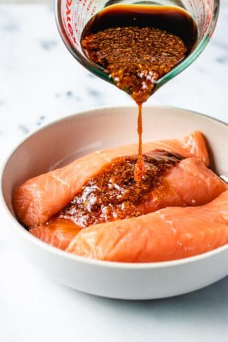 Photo shows pouring the salmon marinade over the fish fillets in plate