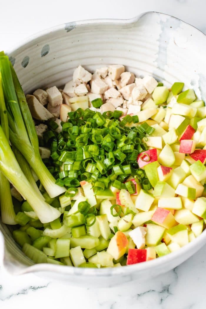 A large mixing bowl with chopped apples, celery, cooked chicken