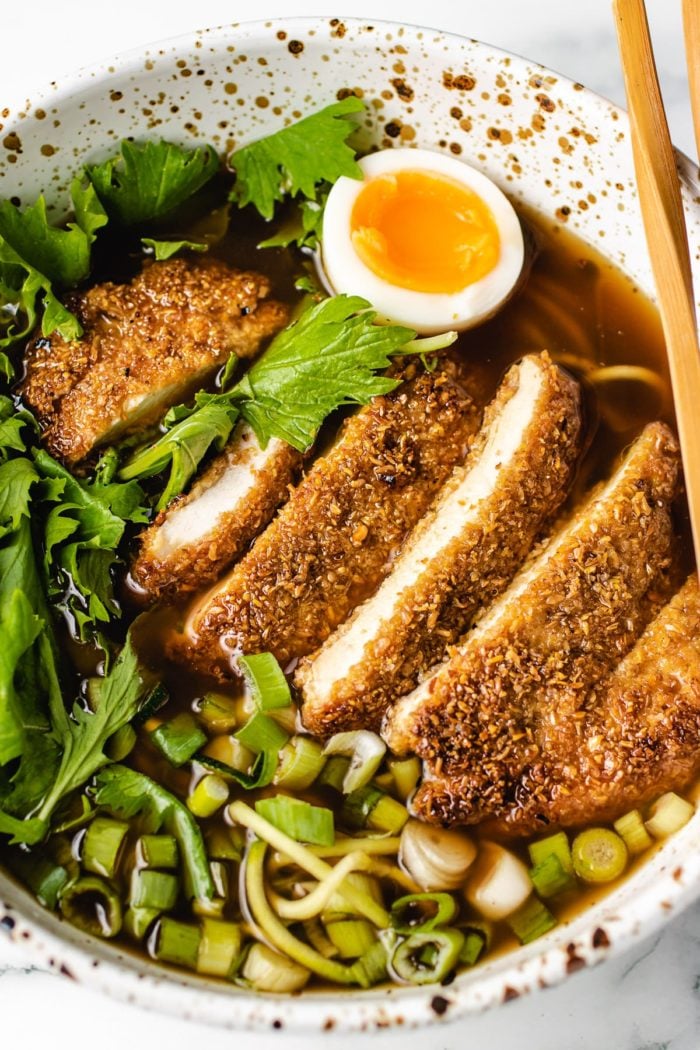 A side shot of katsu chicken in a ramen bowl soup