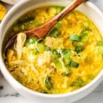 A bowl of chicken egg drop soup, garnished with chopped green onions, with a wooden spoon resting inside, makes for a comforting and healthy egg drop soup option.