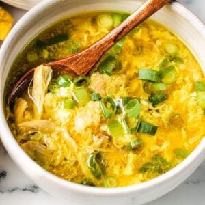 A bowl of chicken egg drop soup, garnished with chopped green onions, with a wooden spoon resting inside, makes for a comforting and healthy egg drop soup option.