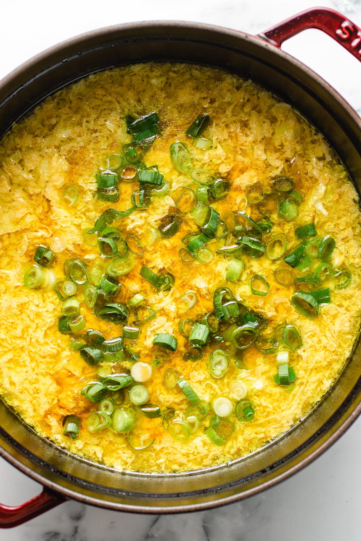 Image shows healthy egg drop soup made in a large pot with chicken and egg flowers.