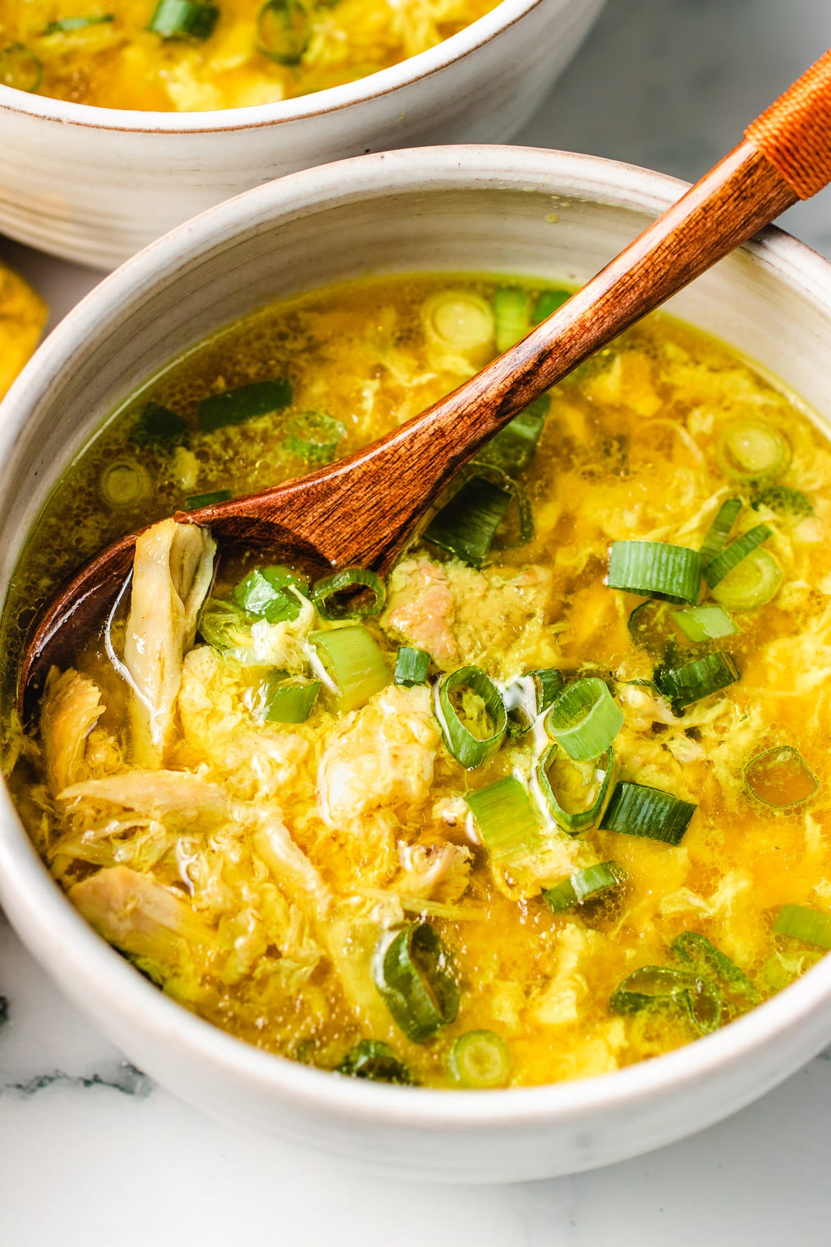 Image shows a white serving bowl with low carb egg drop soup with chicken served in the bowl with a spoon.