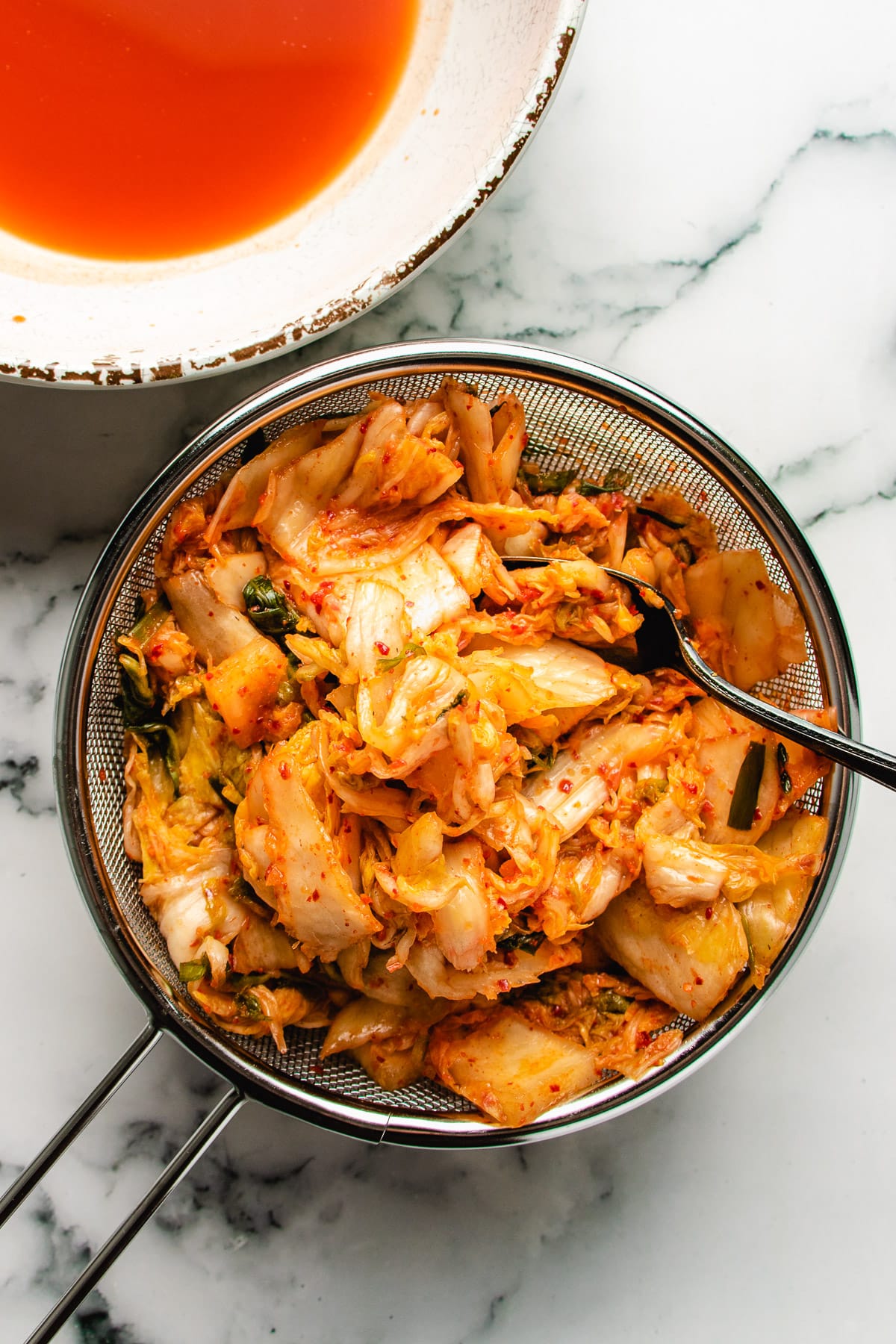 Photo shows draining the kimchi over a sieve and save the kimchi juice in a separate bowl