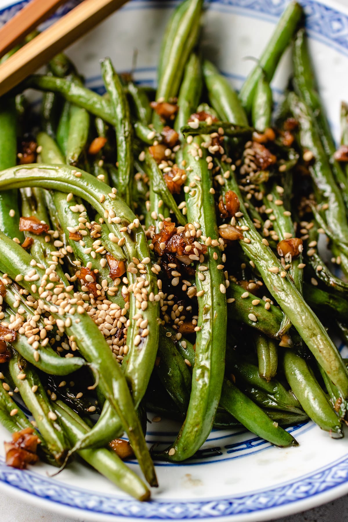 A side close shot photo shows crisp Chinese green beans topped with garlic, soy sauce, and sesame seeds. 