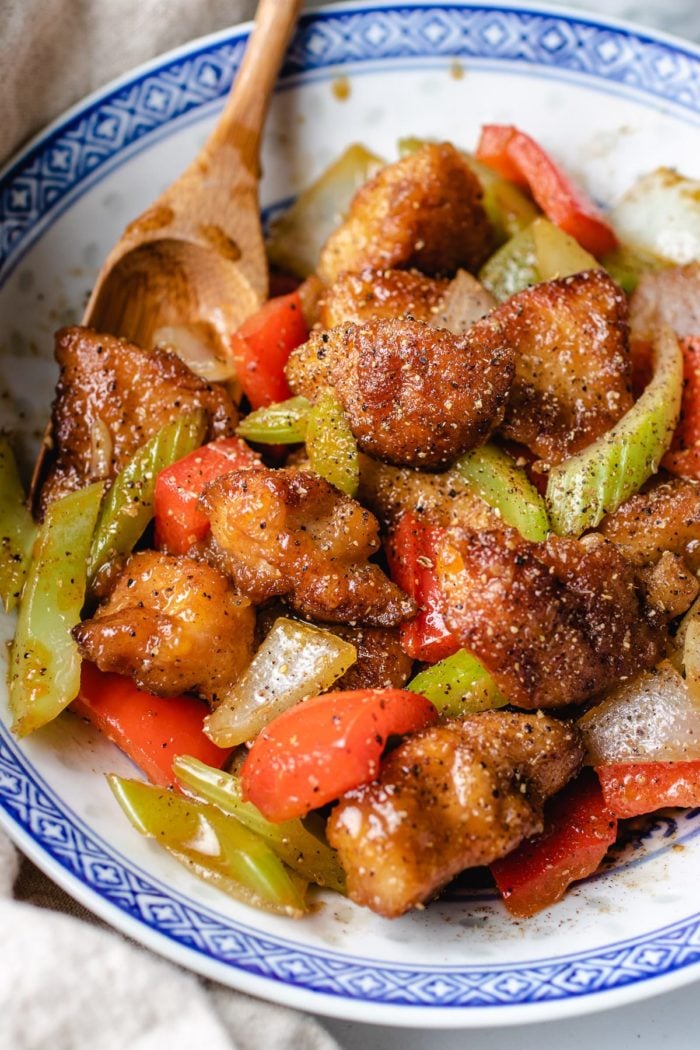 tender chicken breasts stir-fried with peppers and celery in a black pepper sauce served in a blue white color plate. 
