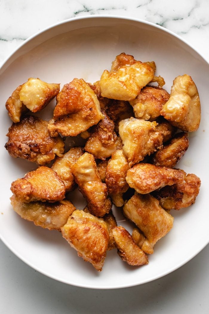 Golden shallow fried cubed chicken breasts on a white plate