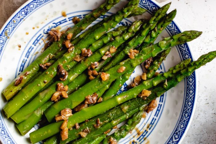 sauteed asparagus seasoned with miso, butter, and garlic, served over a blue white color plate.
