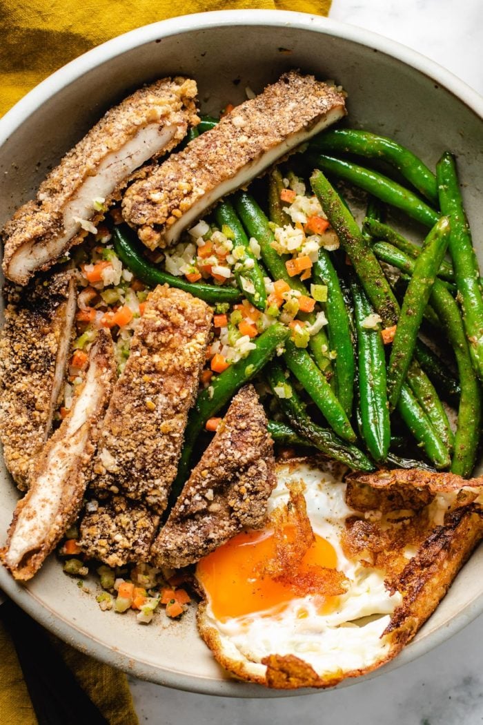 A serving plate with chicken cutlets, eggs, and green beans