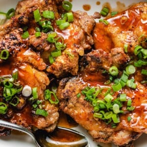 A plate of crispy chicken thighs drizzled with honey sriracha sauce on a white plate