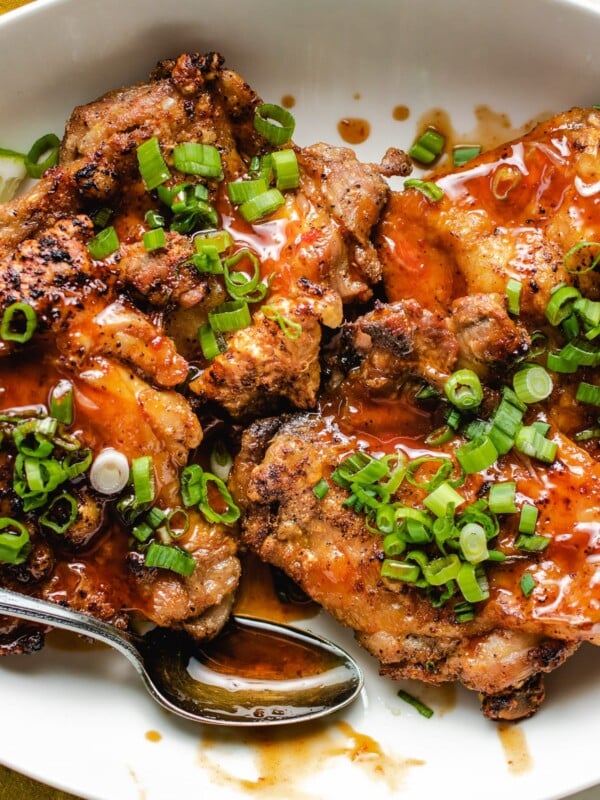 A plate of crispy chicken thighs drizzled with honey sriracha sauce on a white plate