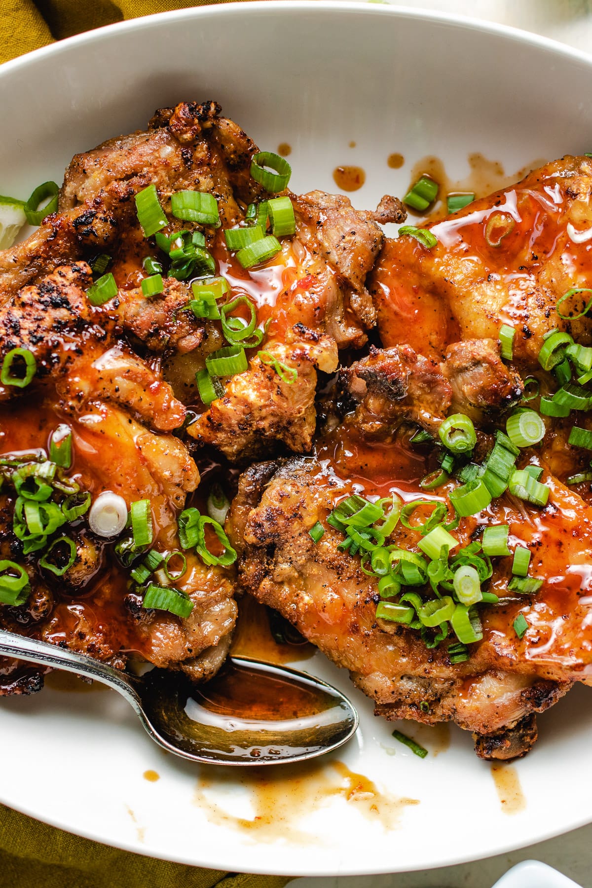 A plate of crispy chicken thighs drizzled with honey sriracha sauce on a white plate