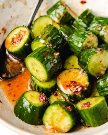 Diced cucumbers tossed in chili honey sauce in a white bowl