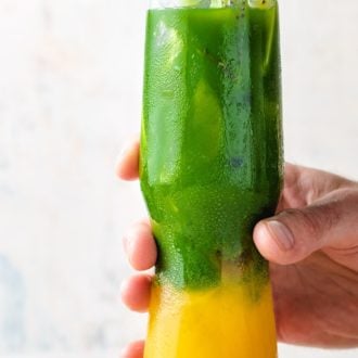 A tall glass filled with Ice, mango juice, and matcha tea