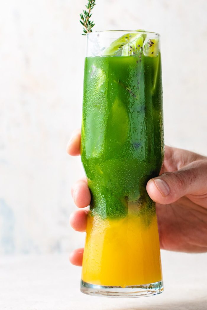 A tall glass filled with Ice, mango juice, and matcha tea