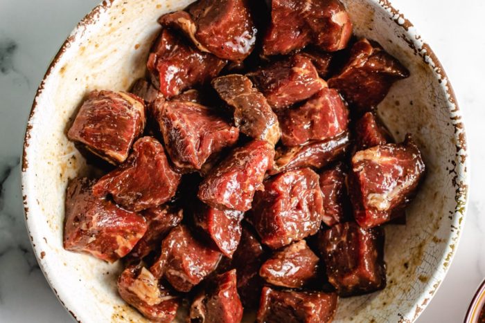 Beef cubes diced up and seasoned with marinade in a white bowl
