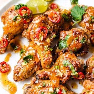 A side shot shows crispy air fryer Vietnamese fish sauce chicken wings with garlic bits and chili pepper on a white plate.