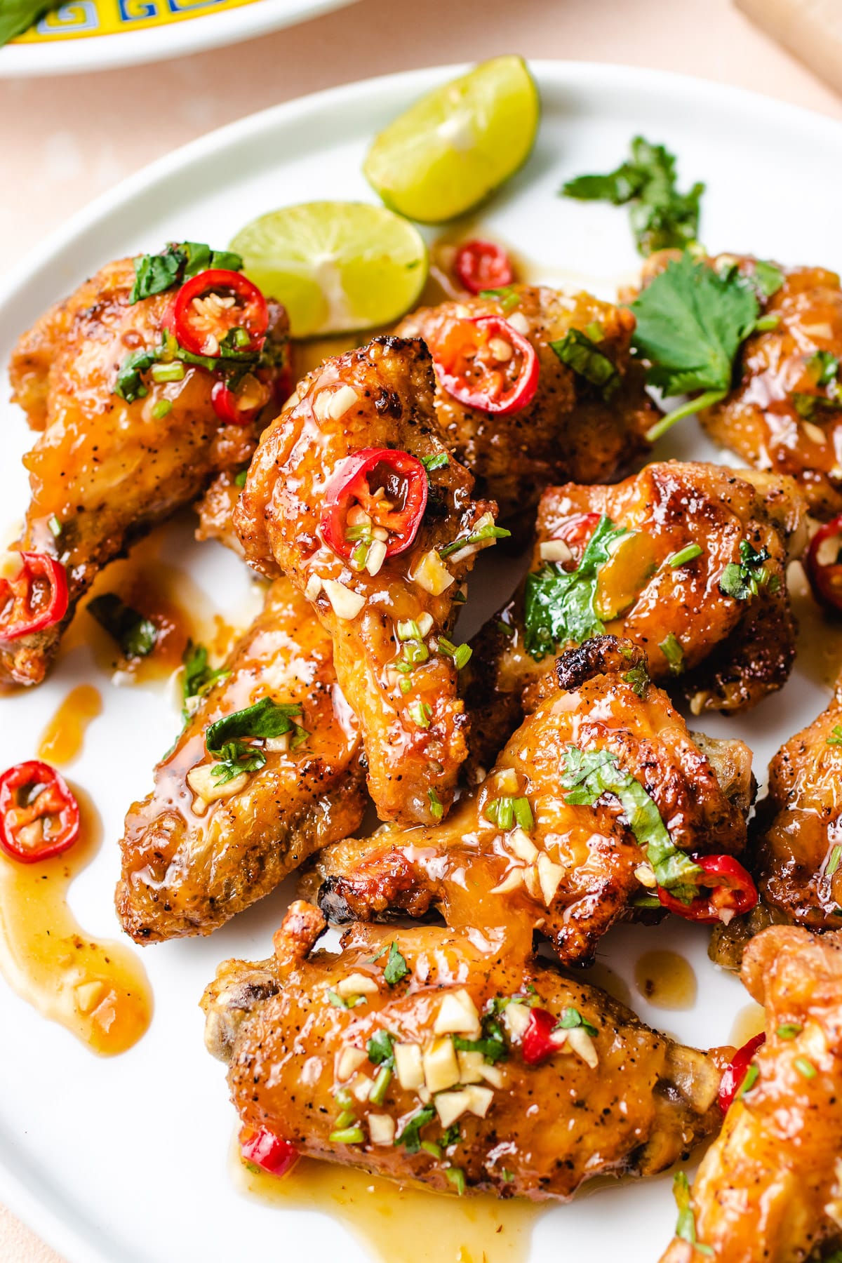 A side shot shows crispy air fryer Vietnamese fish sauce chicken wings with garlic bits and chili pepper on a white plate.