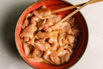 Photo shows thinly sliced chicken breasts and seasoned in a red bowl