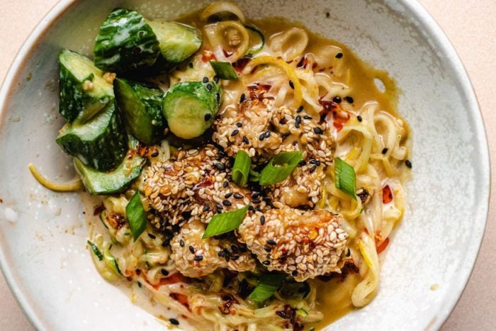 Sesame Chicken with zucchini noodles and cucumbers and sauce in a bowl