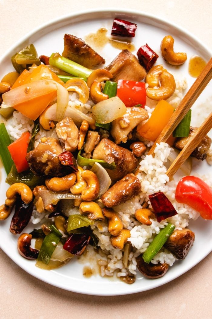 Photo shows serve the stir-fried chicken with cashew nuts over rice on a white plate