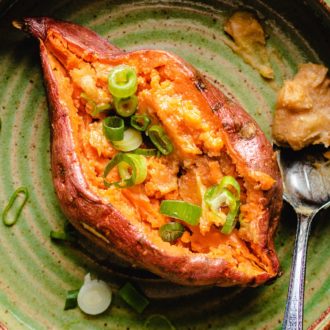 Fluffy baked sweet potatoes with miso butter topping and chopped scallions served on a green plate
