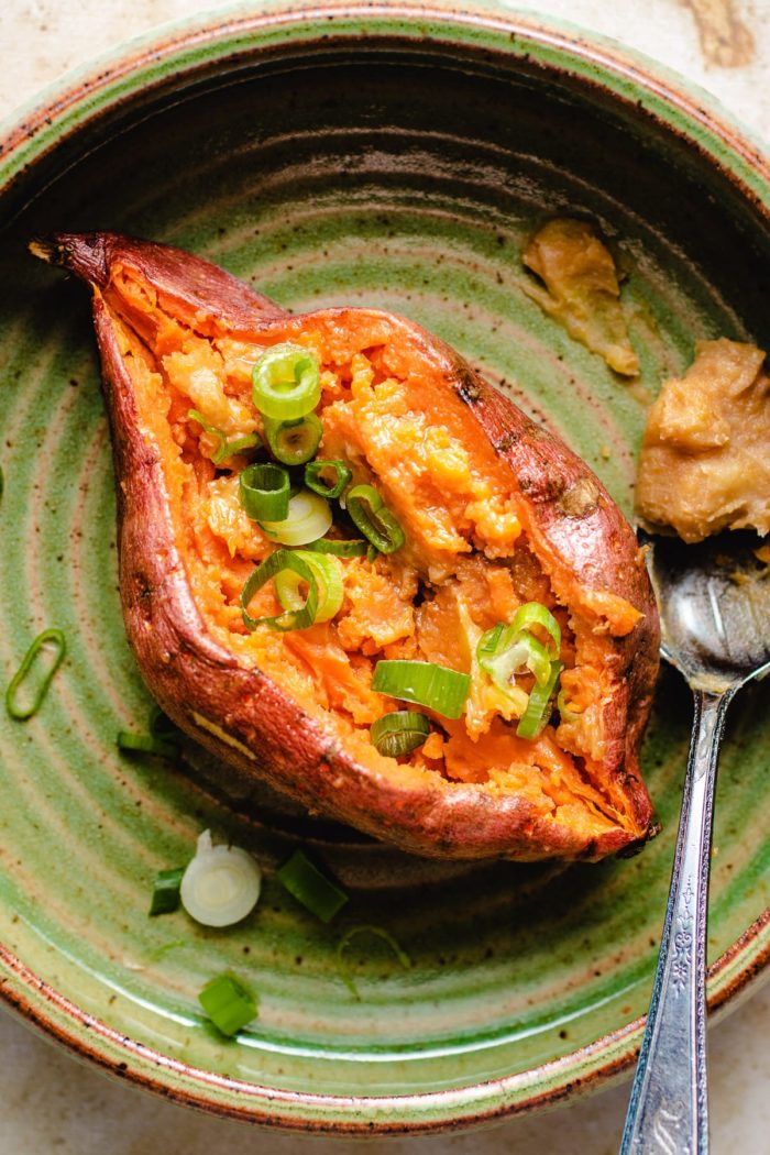 Fluffy baked sweet potatoes with miso butter topping and chopped scallions served on a green plate