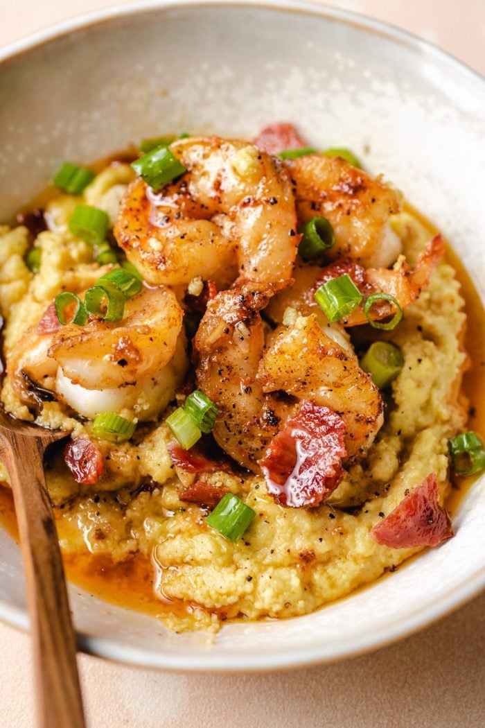 A finishing dish shows serving the shrimp grits with a spoon on the side