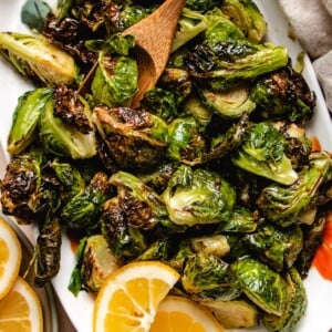 Photo shows a white plate loaded with crispy air fried brussels sprouts glazed with maple lemon sauce and with lemon on the side