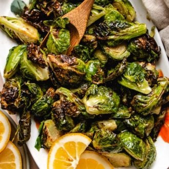 Photo shows a white plate loaded with crispy air fried brussels sprouts with lemon on the side