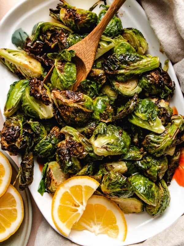 Photo shows a white plate loaded with crispy air fried brussels sprouts glazed with maple lemon sauce and with lemon on the side