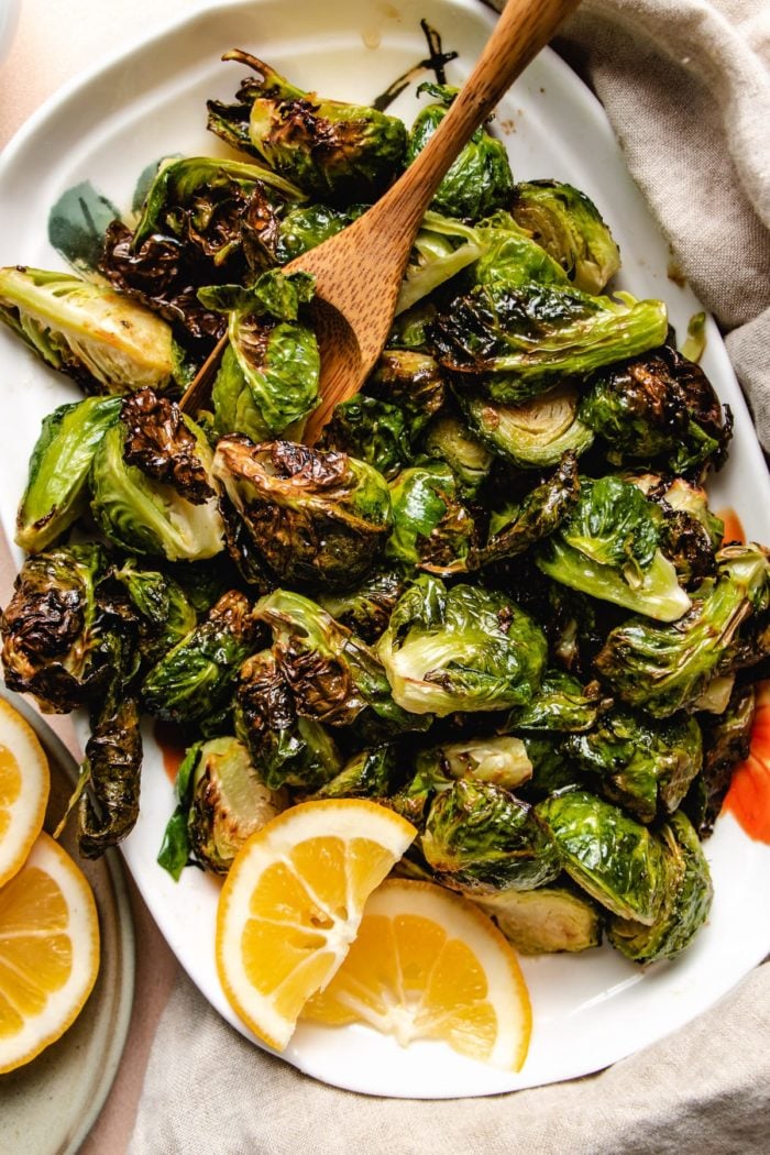 Photo shows a white plate loaded with crispy air fried brussels sprouts with lemon on the side