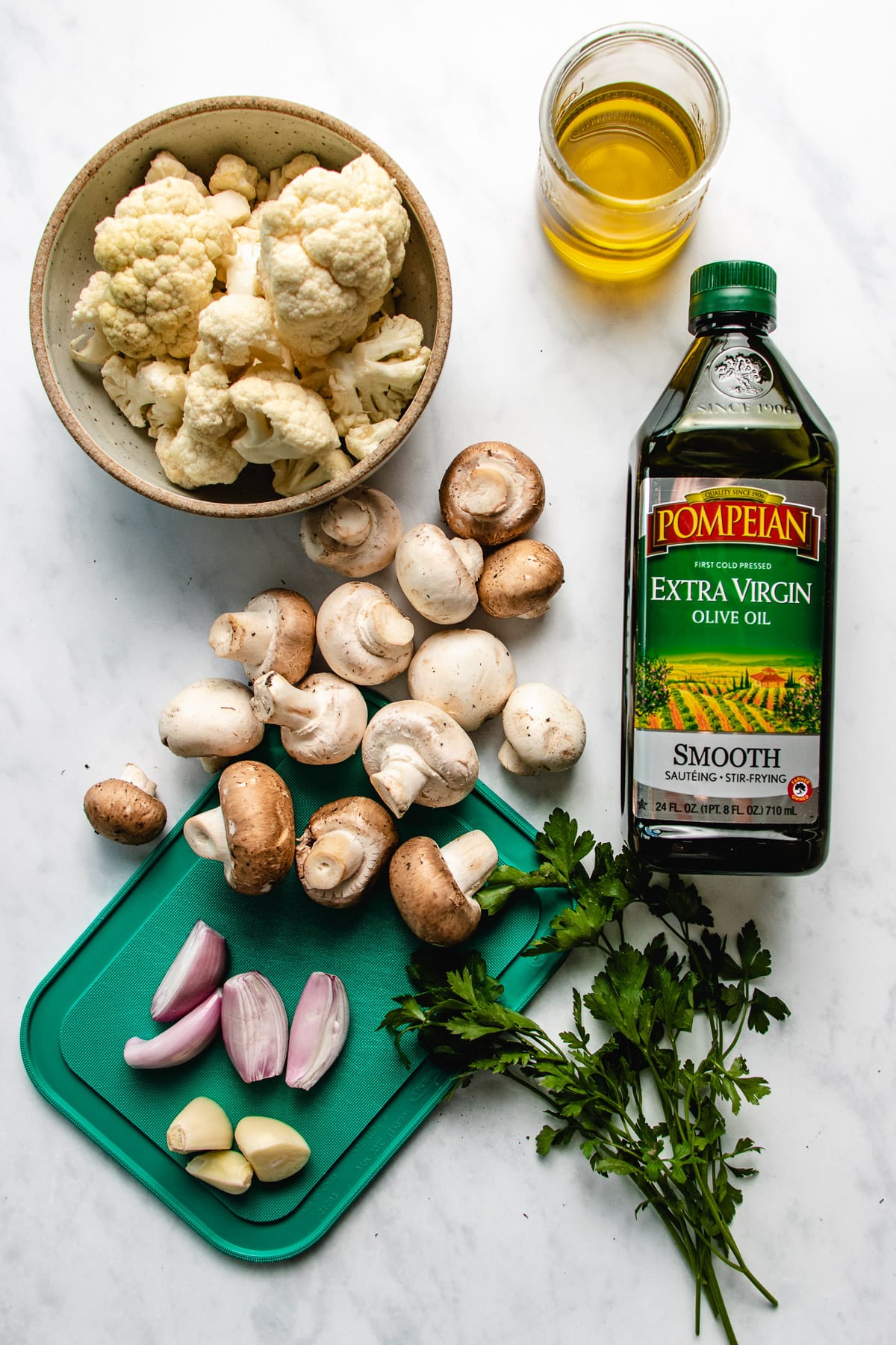 Photo shows ingredients needed to make the dish with mushrooms, cauliflower, garlic, shallot, parsley, and olive oil