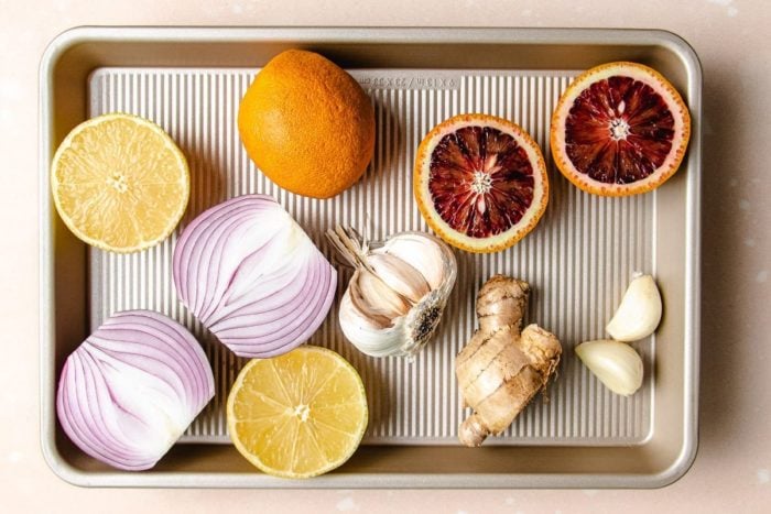 A sheet pan with orange, lemon, ginger, garlic, and onion