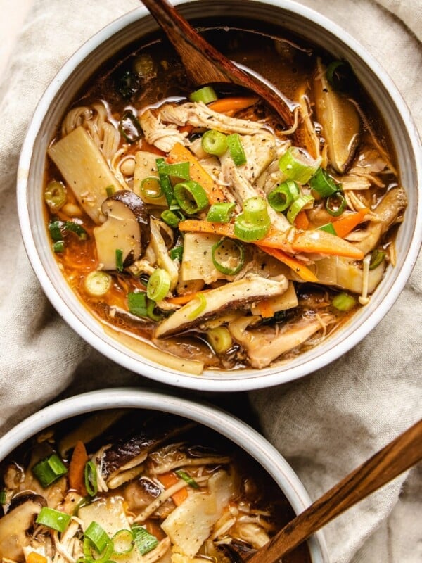 Photo shows two serving white color bowl with Chinese hot sour soup with chicken and serving spoons