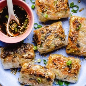 Photo shows pan fried rice wrapper made dumplings with dipping sauce on the side in a light purple plate