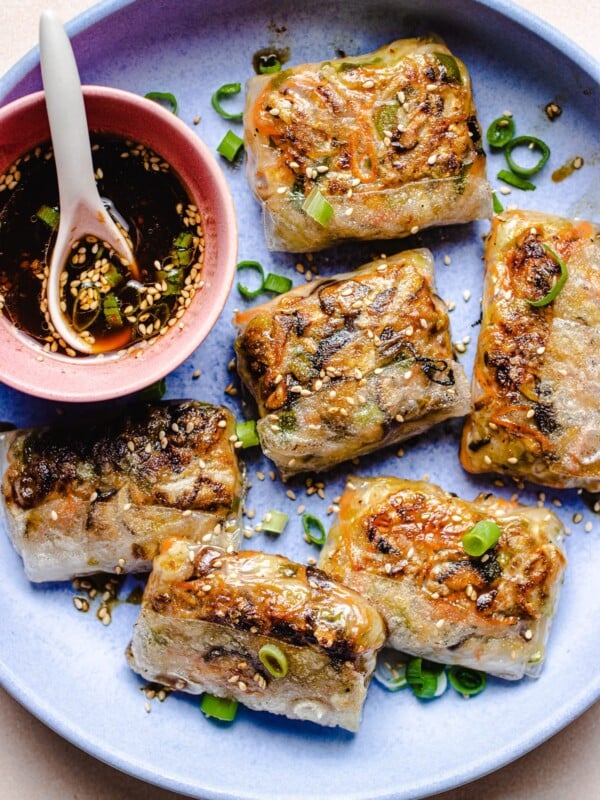 Photo shows pan fried rice wrapper made dumplings with dipping sauce on the side in a light purple plate