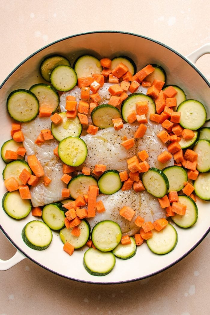 Phot shows diced zucchini and carrots sprinkled around the fish fillets