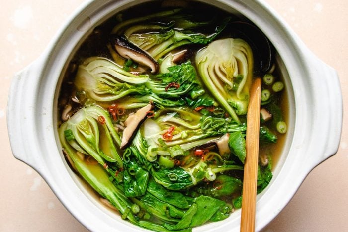 Photo shows a white clay pot with cooked bok choy vegetable in the soup