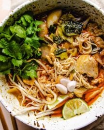 Feature image shows a big white noodle soup bowl with curry chicken, noodles, lime, and cilantro in a creamy coconut red curry milk broth.