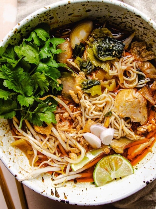 Feature image shows a big white noodle soup bowl with curry chicken, noodles, lime, and cilantro in a creamy coconut red curry milk broth.