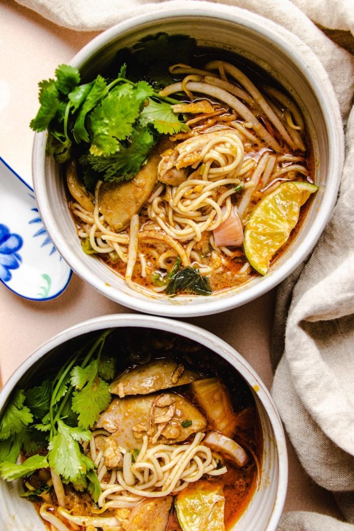 Photo shows two white individual serving bowls with chicken, noodles, and cilantro garnish in Chiang Mai style chicken khao soi soup