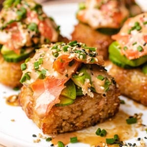 Photo shows 4 pieces of crunchy rice sushi cakes with spicy smoked salmon and garnish on top in a white plate