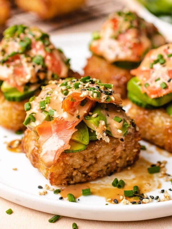 Photo shows 4 pieces of crunchy rice sushi cakes with spicy smoked salmon and garnish on top in a white plate