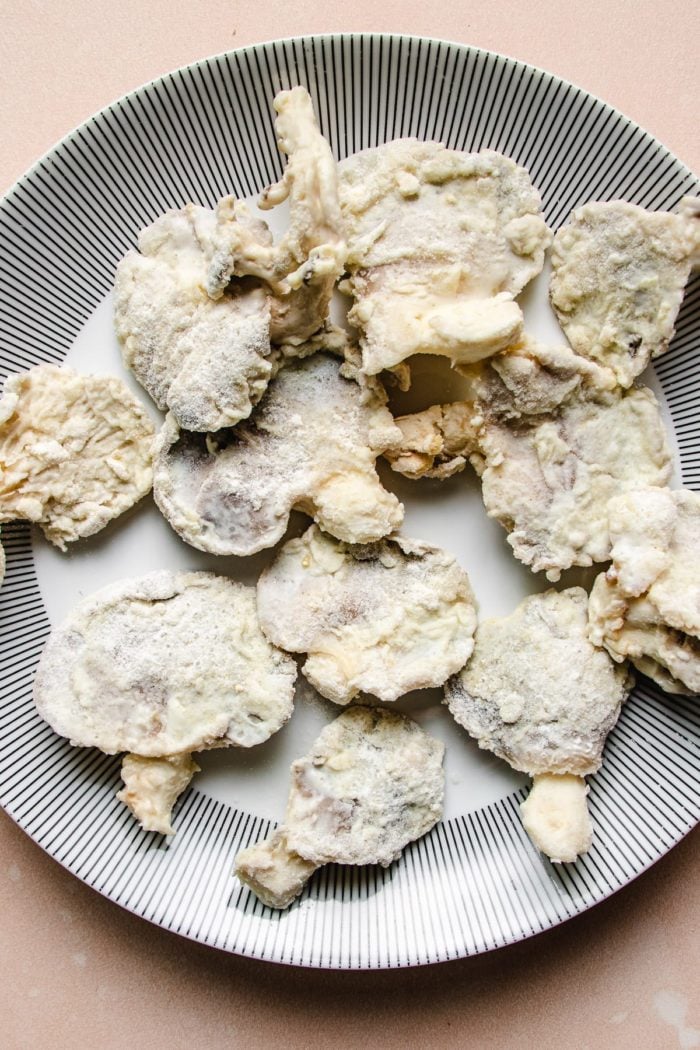 Photo shows mushrooms coated with starch and flour ready to air fry on a large plate