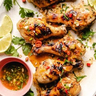 Photo shows 6 grilled chicken legs drizzled with sauce on a big white oval plate